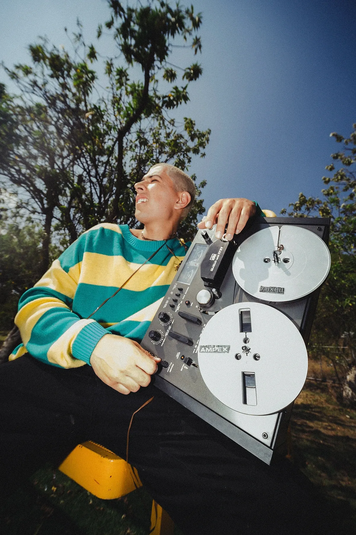 Galo Barker sentado al aire libre sosteniendo una grabadora de carrete contra el cielo